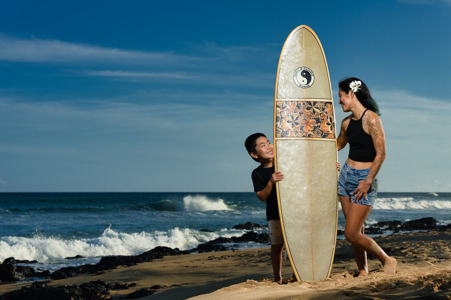 Oahu Photographer for Honolulu Family Ohana Portraits Photography A Honolulu photographer captures family ohana portraits on an Oahu beach. A mother and son pose with a surfboard for professional beach photography at sunset.