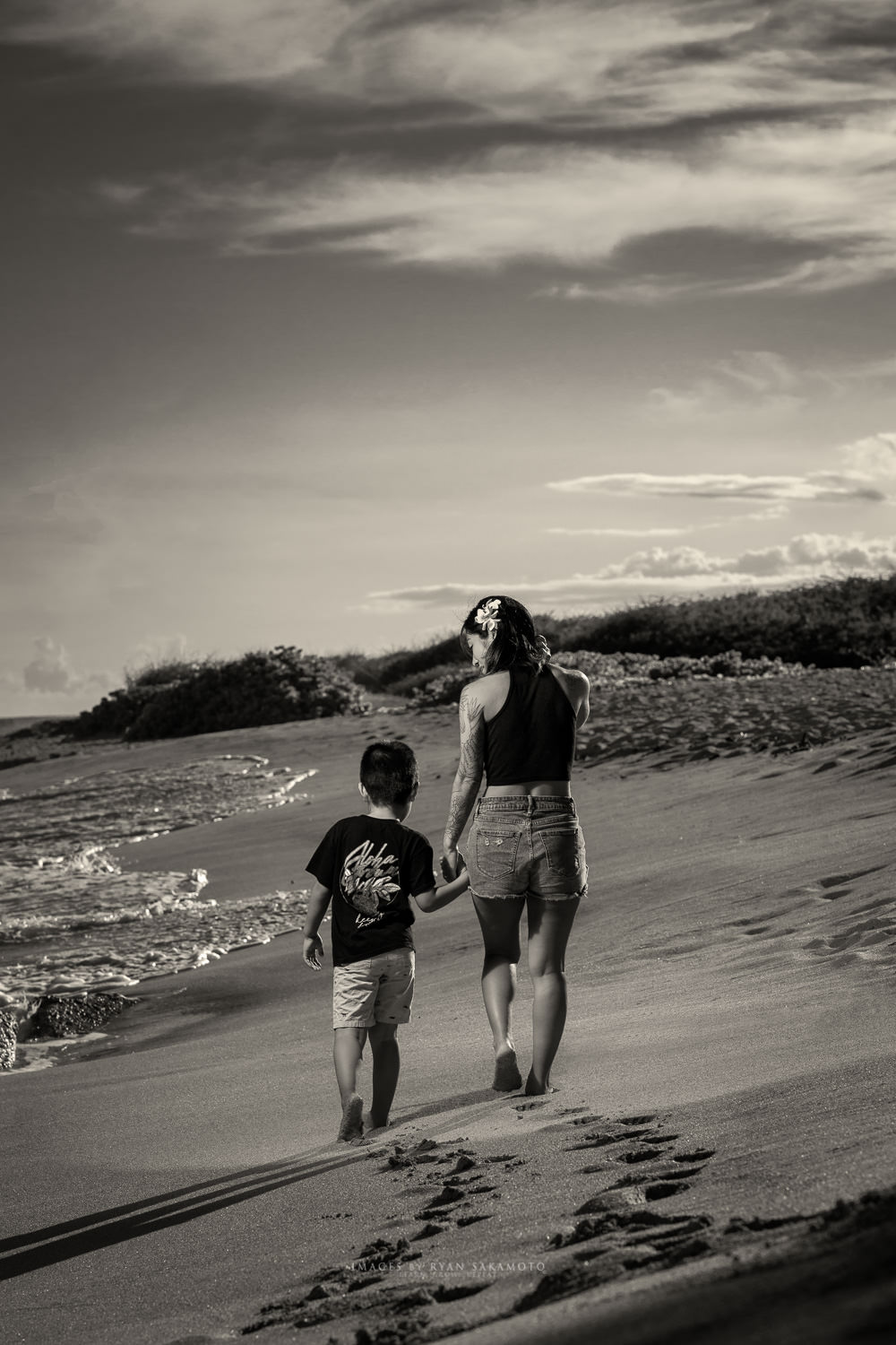 Honolulu Family Ohana Portraits Photography Oahu Photographer Black and white photography of a mother and son walking on an Oahu beach. A Honolulu photographer captures family ohana portraits along the sandy shoreline.