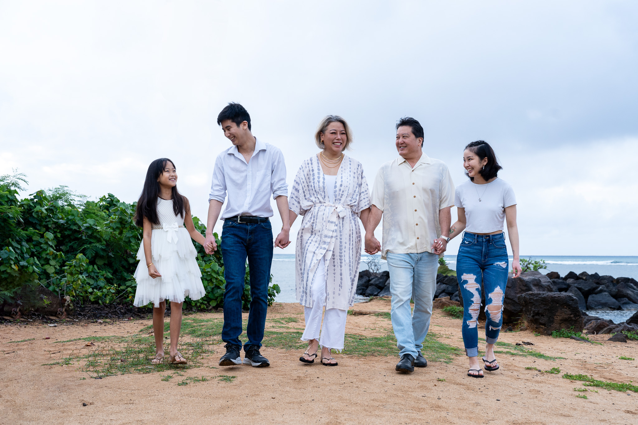 Oahu Photographer for Honolulu Family Ohana Portraits Photography A Honolulu photographer captures family ohana portraits on Oahu. A smiling family of five walks hand-in-hand along the beach during a professional photography session.