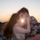 Close-up of a couple kissing on a rocky beach at sunset during an Oahu creative photo session, with golden sunlight catching the woman's flowing hair.