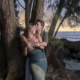 Man embracing his fiancée from behind and kissing her cheek under coastal trees on Oahu.